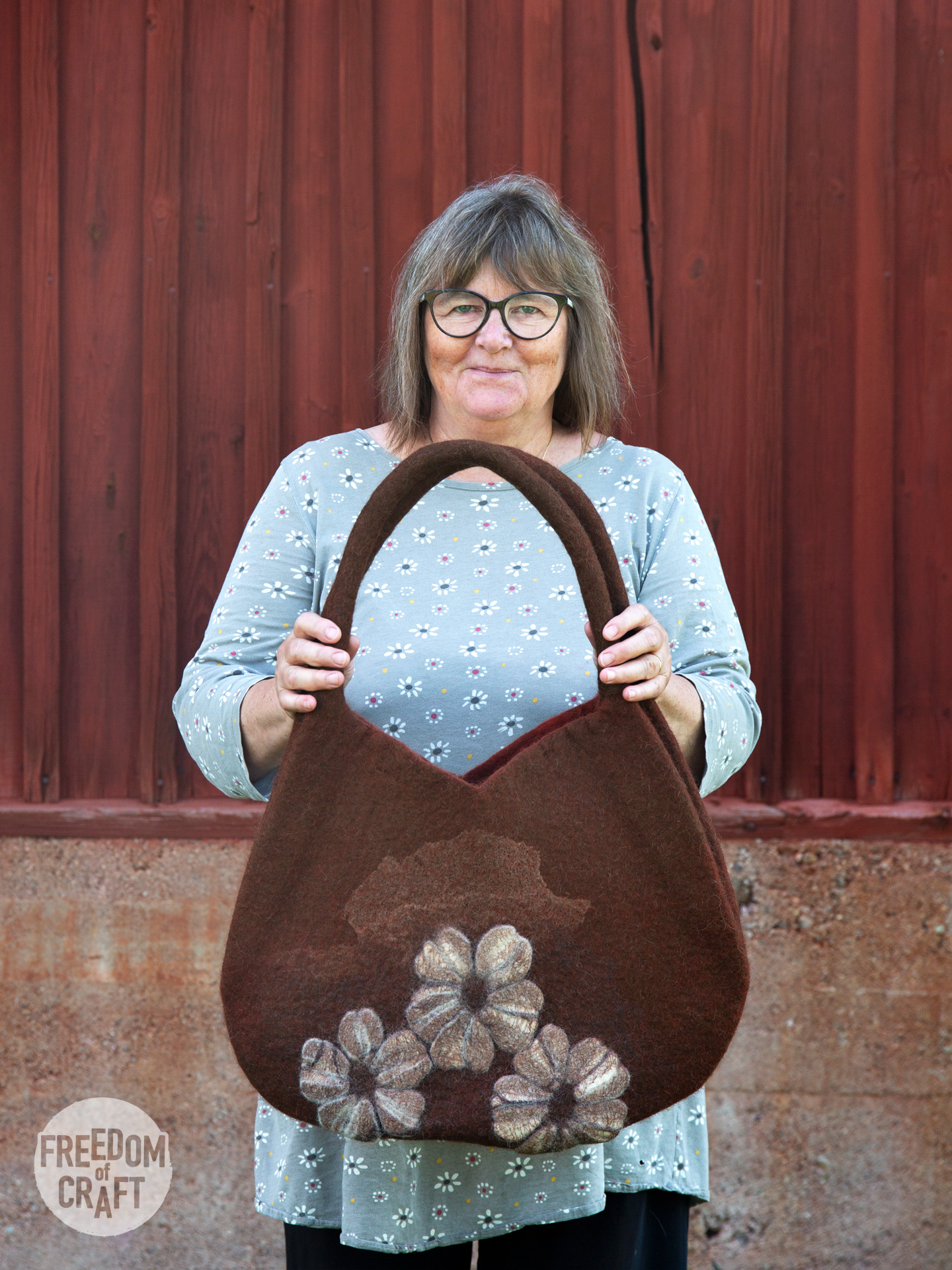 A woman holding up a brown bag adorned with white flowers, smiling with satisfaction.